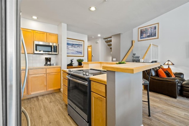 kitchen with a breakfast bar, tasteful backsplash, appliances with stainless steel finishes, open floor plan, and light wood-type flooring