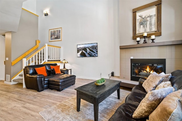 living area featuring a tile fireplace, a high ceiling, wood finished floors, baseboards, and stairway