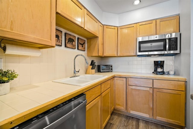 kitchen featuring tile counters, backsplash, appliances with stainless steel finishes, dark wood-type flooring, and a sink