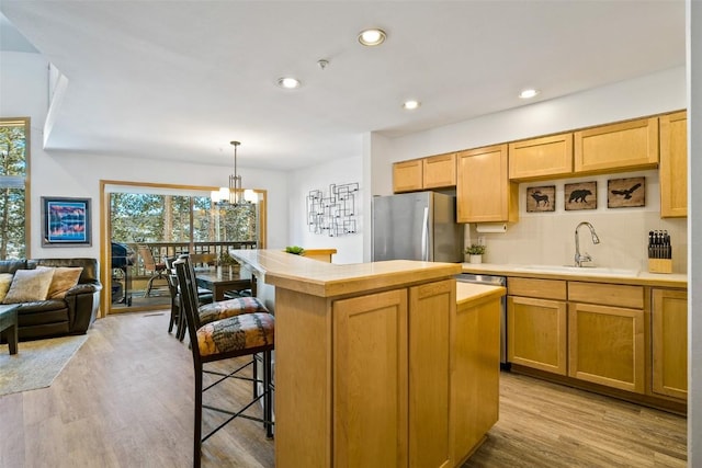 kitchen with light wood finished floors, a center island, freestanding refrigerator, a sink, and recessed lighting