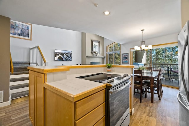 kitchen with stainless steel appliances, a center island, tile counters, and light wood-style floors