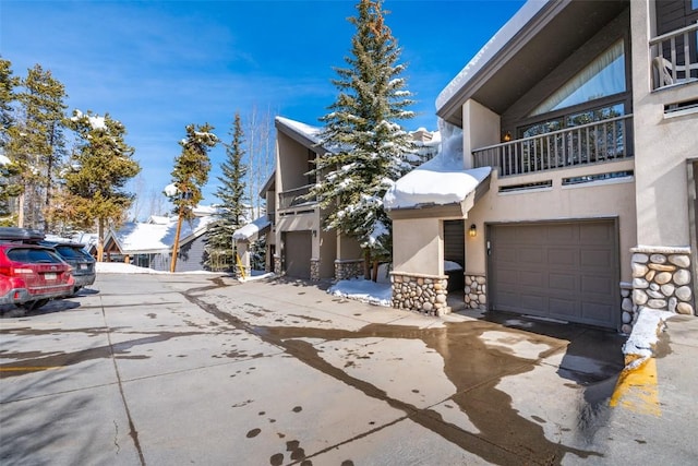 exterior space featuring a balcony, a garage, driveway, stone siding, and stucco siding