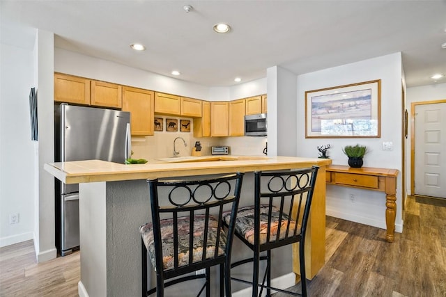 kitchen featuring a breakfast bar area, recessed lighting, light brown cabinetry, appliances with stainless steel finishes, and wood finished floors