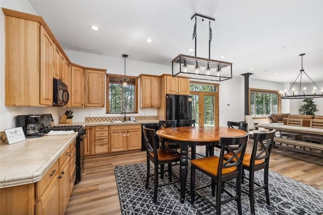 kitchen with pendant lighting, sink, black appliances, and light hardwood / wood-style floors