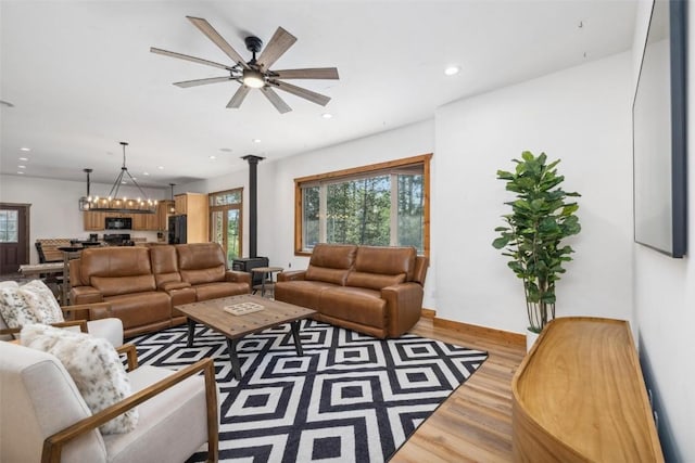 living room with ceiling fan with notable chandelier and light hardwood / wood-style flooring