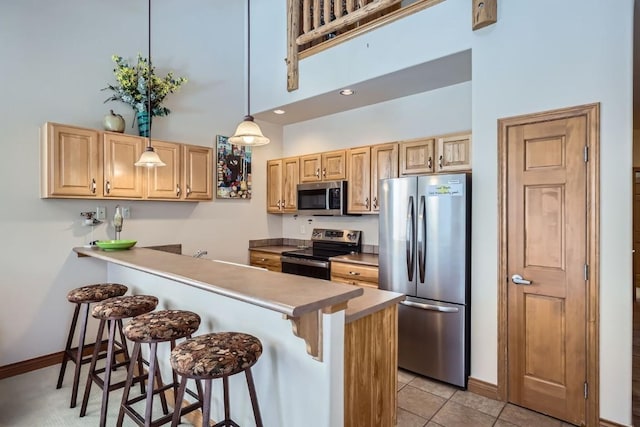 kitchen featuring light brown cabinets, a peninsula, a high ceiling, appliances with stainless steel finishes, and a kitchen breakfast bar