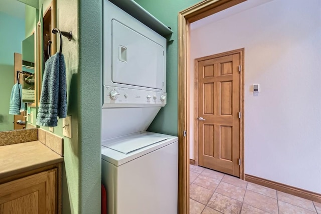 laundry room featuring light tile patterned floors, laundry area, stacked washing maching and dryer, and baseboards