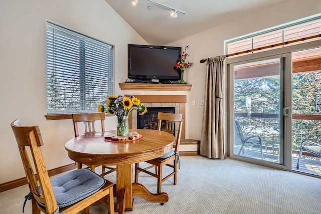 dining room with a tiled fireplace, carpet floors, baseboards, and vaulted ceiling