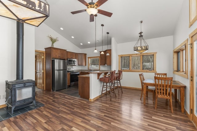 kitchen featuring hanging light fixtures, stainless steel appliances, a kitchen bar, kitchen peninsula, and a wood stove