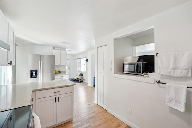 kitchen with stainless steel appliances, light wood-style floors, a peninsula, and white cabinetry