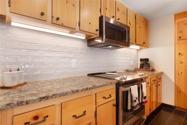 kitchen featuring light stone counters, dark tile patterned flooring, baseboards, appliances with stainless steel finishes, and backsplash