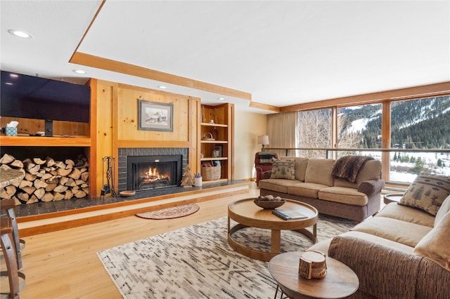 living area with a warm lit fireplace, built in shelves, wood finished floors, and recessed lighting