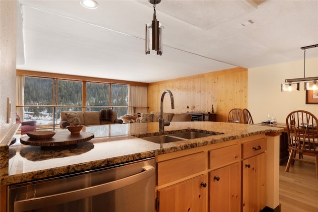 kitchen featuring light wood finished floors, stone countertops, decorative light fixtures, a sink, and stainless steel dishwasher