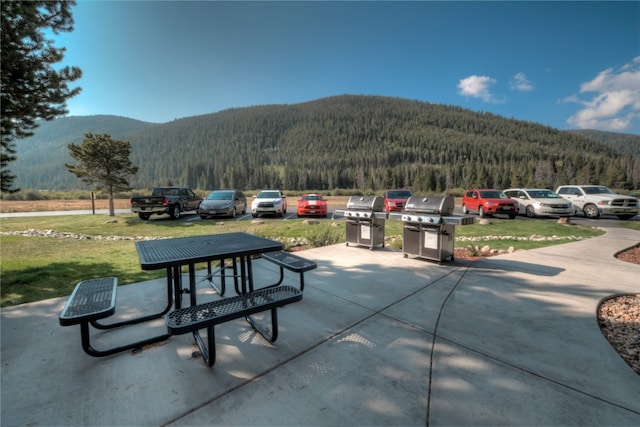 surrounding community with a forest view, a mountain view, a lawn, and a patio