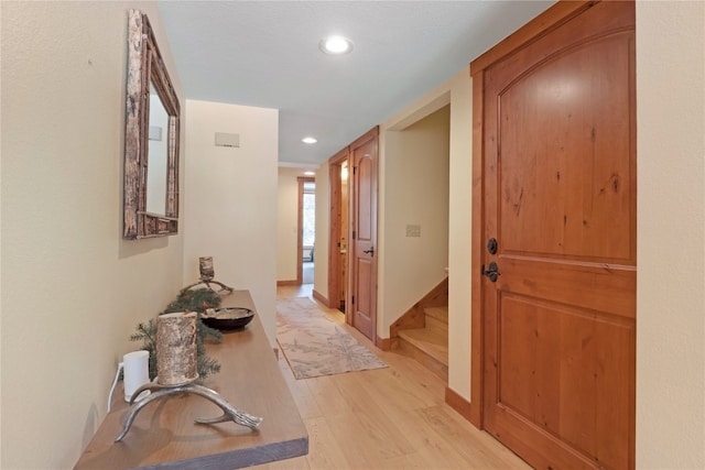 hall featuring light wood-style floors, recessed lighting, baseboards, and stairs