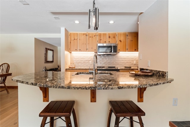 kitchen with tasteful backsplash, stainless steel microwave, light wood-style floors, a sink, and dark stone counters