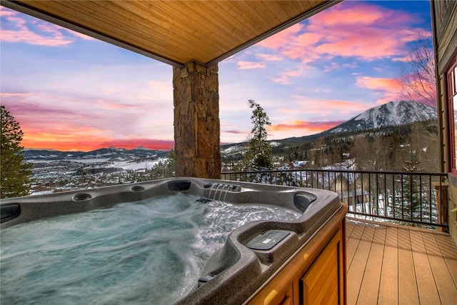 snow covered deck with a mountain view and a hot tub