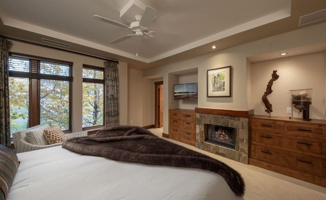 bedroom with a raised ceiling, a stone fireplace, and ceiling fan