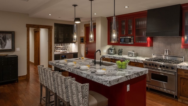 kitchen featuring appliances with stainless steel finishes, decorative light fixtures, an island with sink, sink, and custom exhaust hood