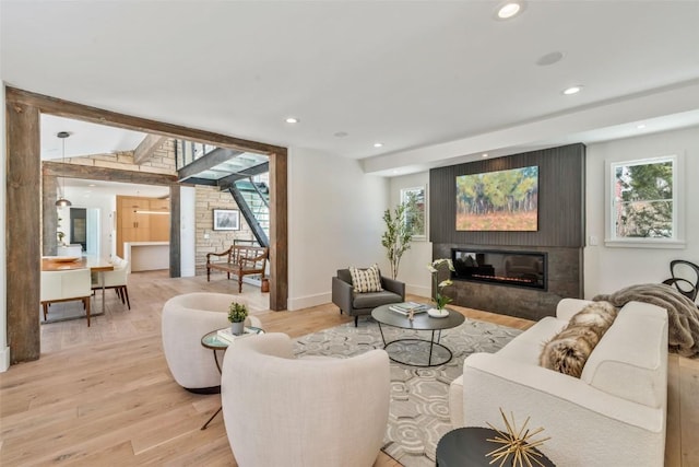 living room with vaulted ceiling with beams, recessed lighting, baseboards, light wood finished floors, and a glass covered fireplace