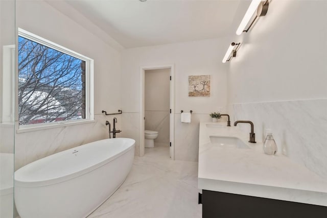 bathroom with toilet, a sink, marble finish floor, a freestanding tub, and tile walls