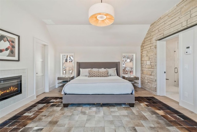 bedroom with a glass covered fireplace, vaulted ceiling, and baseboards