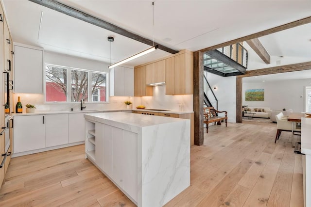 kitchen featuring light wood finished floors, modern cabinets, pendant lighting, and beam ceiling