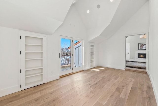 interior space with lofted ceiling, baseboards, light wood-style floors, access to outside, and a glass covered fireplace