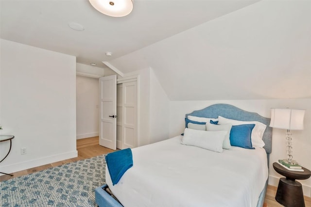 bedroom with vaulted ceiling, baseboards, and wood finished floors