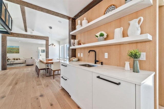 kitchen featuring light wood finished floors, white cabinets, vaulted ceiling with beams, open shelves, and a sink