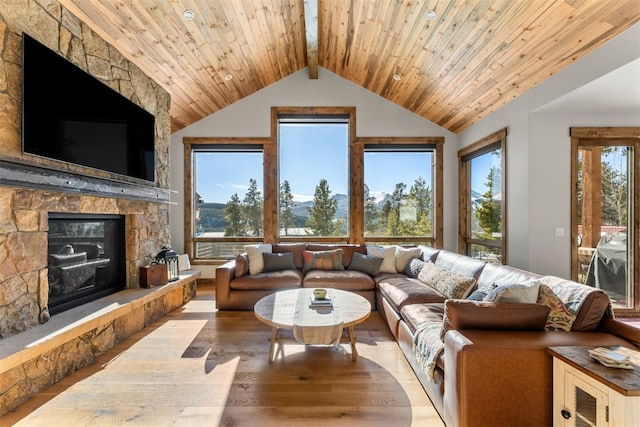 living room with a stone fireplace, a wealth of natural light, lofted ceiling with beams, wooden ceiling, and light hardwood / wood-style flooring