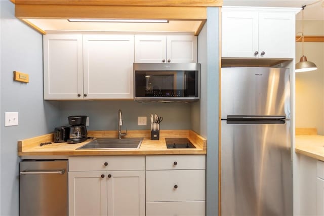 kitchen featuring appliances with stainless steel finishes, butcher block counters, white cabinets, and a sink