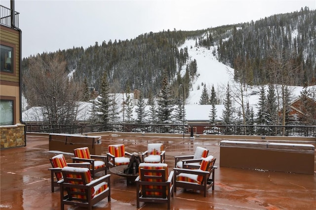 snow covered patio with a mountain view, a hot tub, and a forest view