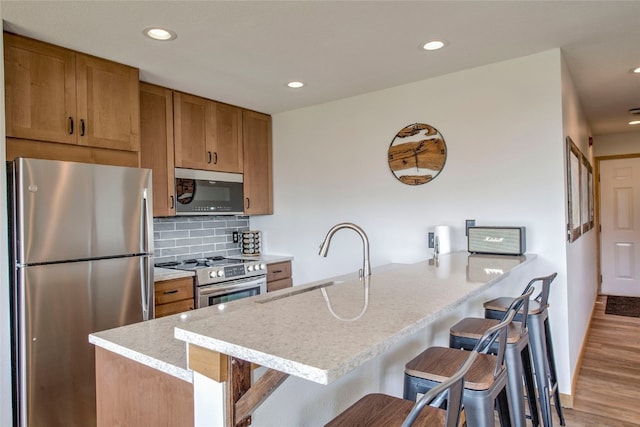 kitchen featuring sink, a breakfast bar, backsplash, stainless steel appliances, and kitchen peninsula