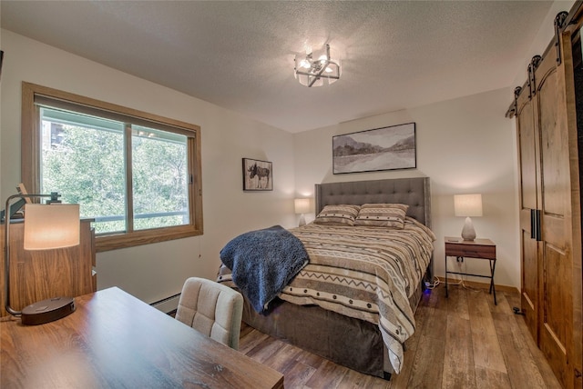 bedroom featuring wood-type flooring, a barn door, a baseboard heating unit, and a textured ceiling