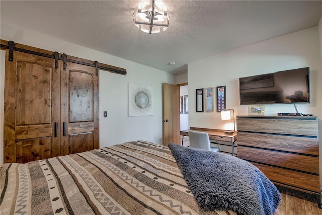 bedroom featuring wood-type flooring, a barn door, and a textured ceiling