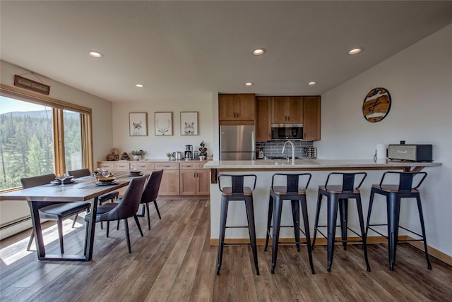 kitchen with a breakfast bar, sink, tasteful backsplash, light hardwood / wood-style flooring, and appliances with stainless steel finishes