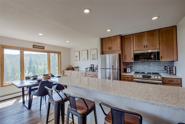 kitchen featuring appliances with stainless steel finishes, tasteful backsplash, a breakfast bar area, light stone counters, and light wood-type flooring