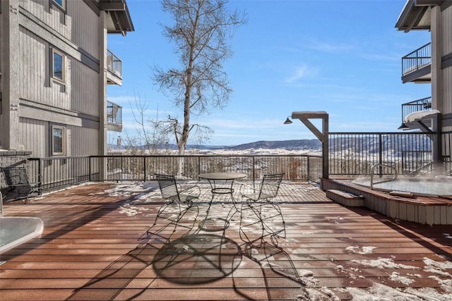 snow covered deck with hot tub deck surround, a mountain view, and outdoor dining space