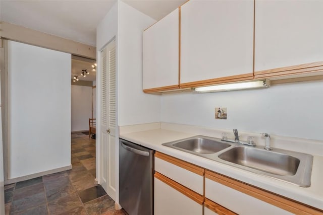 kitchen featuring white cabinets, stone finish flooring, light countertops, stainless steel dishwasher, and a sink