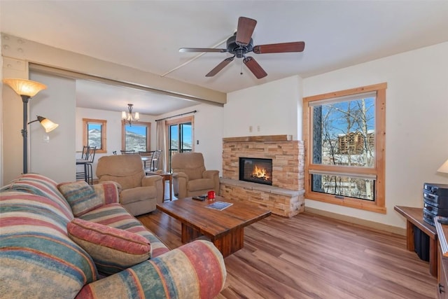 living area featuring light wood-style floors, ceiling fan with notable chandelier, and a stone fireplace