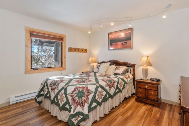 bedroom with a baseboard radiator, wood finished floors, rail lighting, and baseboards