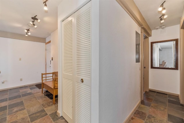 corridor with stone finish floor, rail lighting, and baseboards