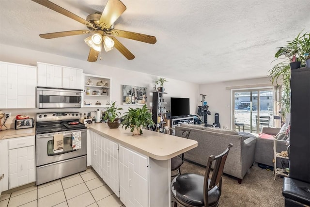 kitchen with stainless steel appliances, light tile patterned floors, kitchen peninsula, a breakfast bar area, and white cabinets