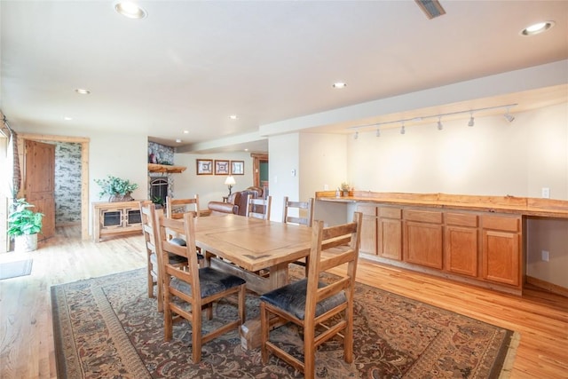 dining room featuring a fireplace, light wood-type flooring, and track lighting