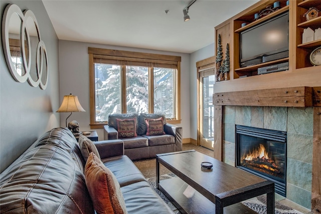 living room featuring a tiled fireplace, rail lighting, and baseboards