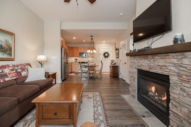 living room featuring a fireplace, ceiling fan, and dark wood-type flooring