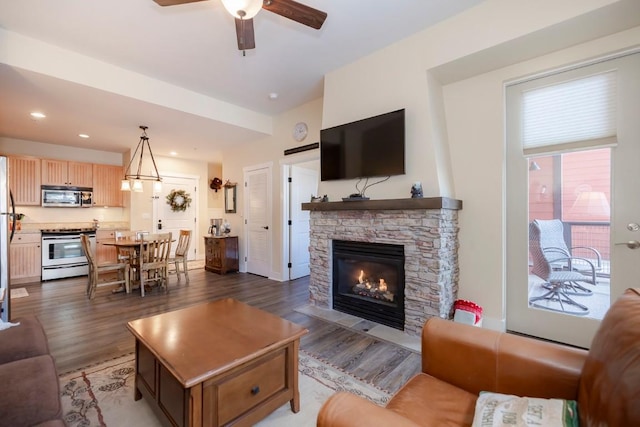 living room featuring dark hardwood / wood-style floors, ceiling fan, and a stone fireplace