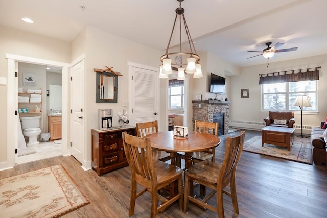 dining space with light wood-type flooring, ceiling fan with notable chandelier, a baseboard radiator, and a fireplace