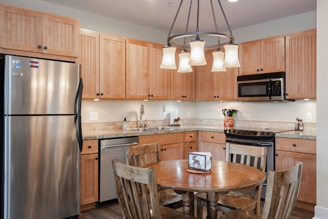 kitchen featuring light stone countertops, light brown cabinetry, stainless steel appliances, sink, and pendant lighting